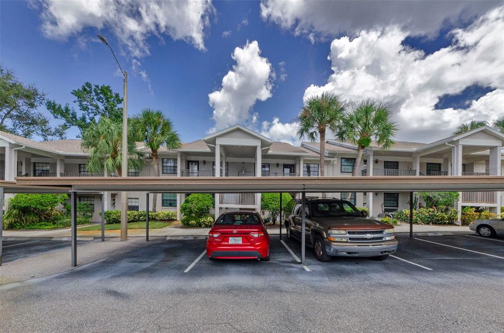 A two-story apartment building exterior with a covered parking area in the foreground — 2119 ELM STREET UNIT 103, DUNEDIN, FL