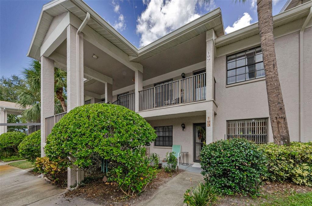 A two-story residential building exterior with a ground-level patio and an upper-level balcony — 2119 ELM STREET UNIT 103, DUNEDIN, FL