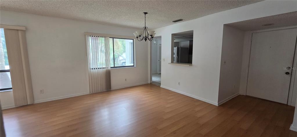 An empty living room features wood-look flooring, a chandelier, a window with blinds, and a pass-through — 700 STARKEY RD UNIT 1224, LARGO, FL