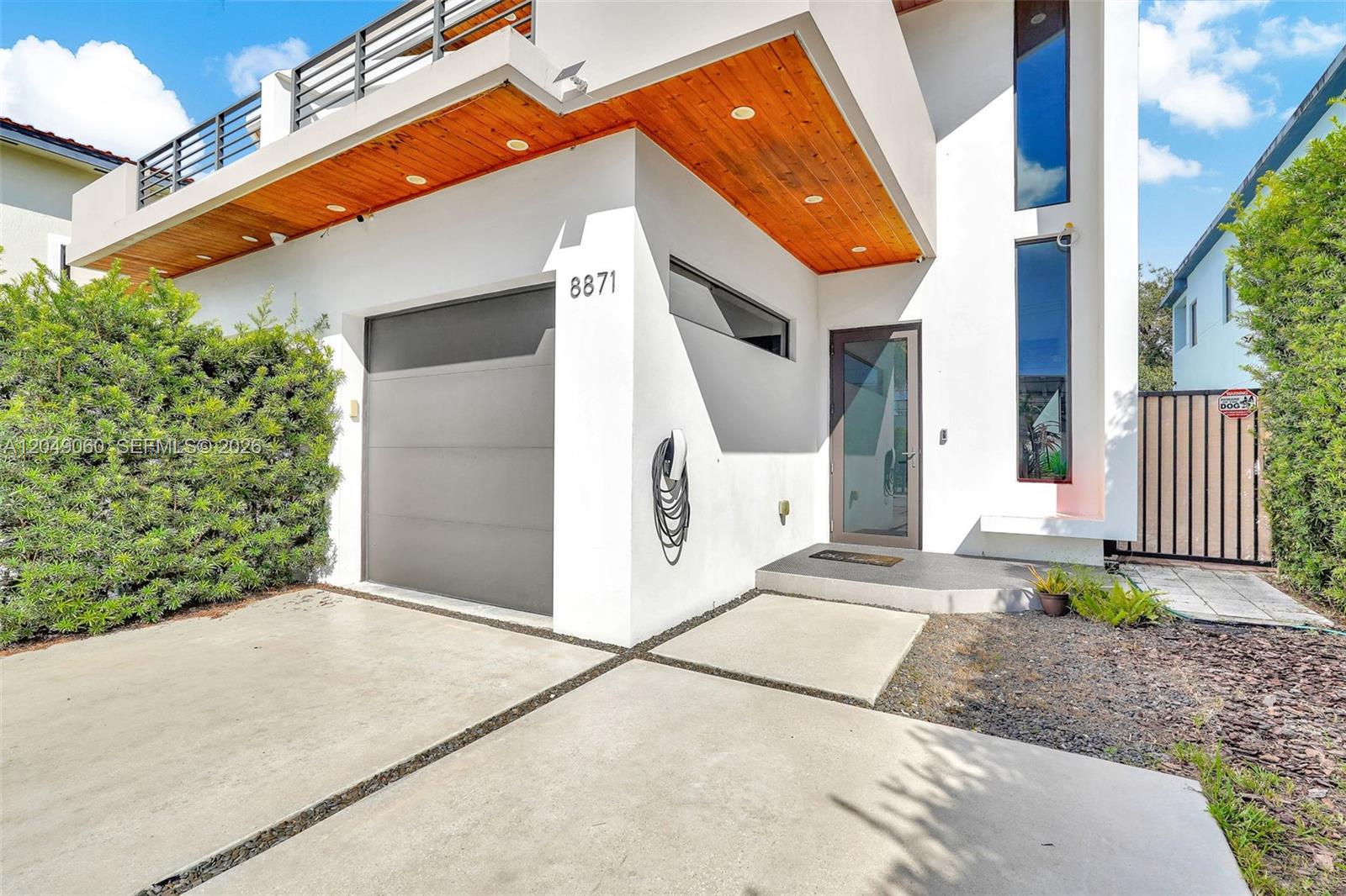 The exterior of a modern white house features a garage, wood-paneled overhang, and glass door — 8871 SW 28th St, Miami FL 33165, MIAMI, FL