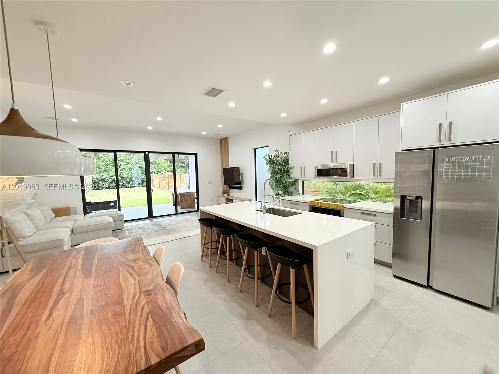 A modern kitchen features a white island, stainless steel appliances, and a wooden dining table — 8871 SW 28th St, Miami FL 33165, MIAMI, FL