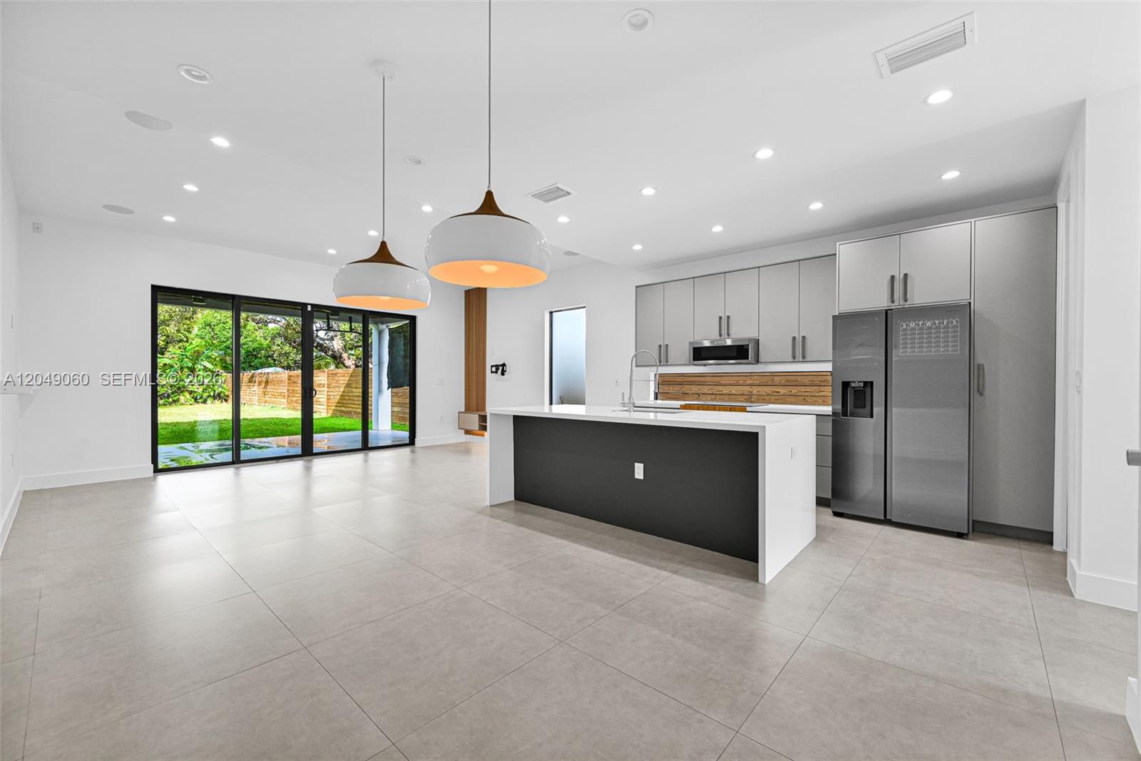 A modern kitchen features a dark island, gray cabinetry, and sliding glass doors to a yard — 8871 SW 28th St, Miami FL 33165, MIAMI, FL