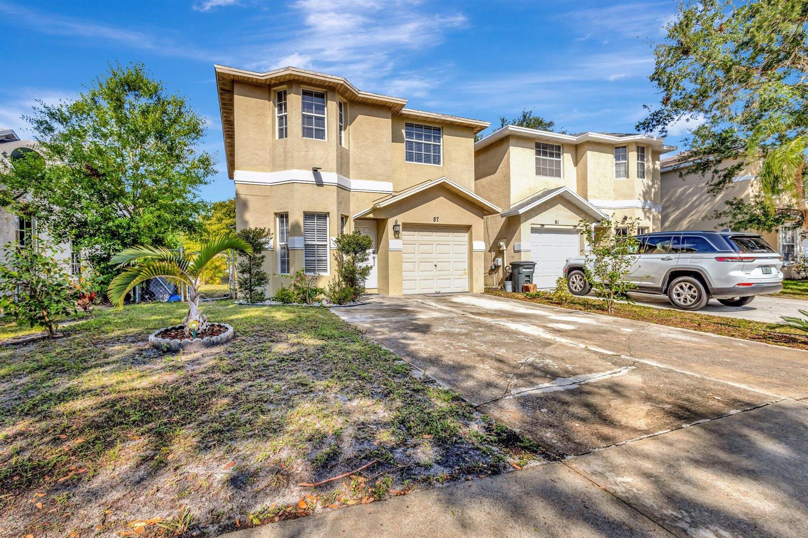 A two-story tan stucco duplex with a concrete driveway and a silver SUV parked outside — 87 Pheasant Run Boulevard, West Palm Beach FL 33415, WEST PALM BEACH, FL