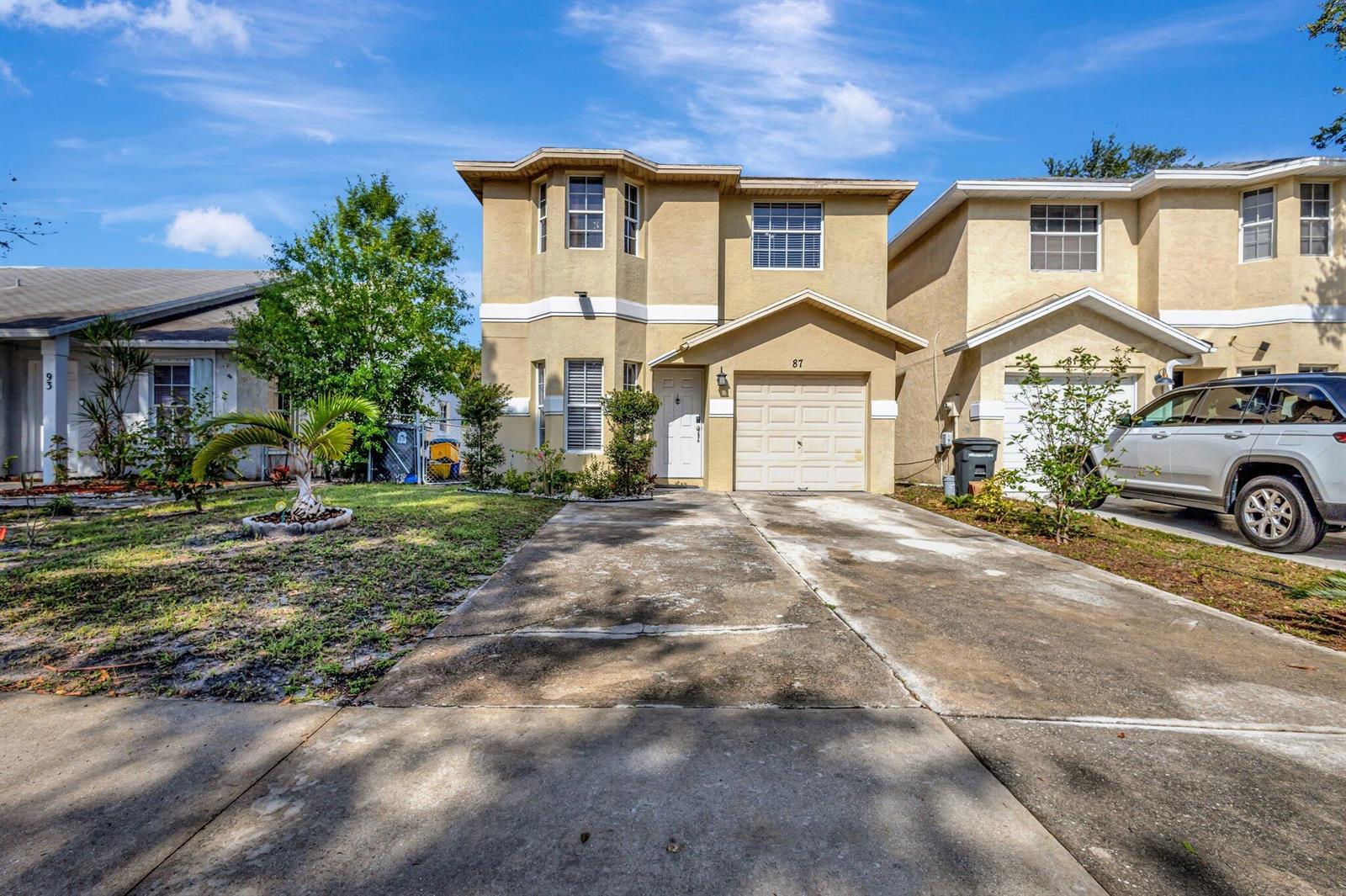 A two-story tan stucco house with a concrete driveway and a single-car garage — 87 Pheasant Run Boulevard, West Palm Beach FL 33415, WEST PALM BEACH, FL