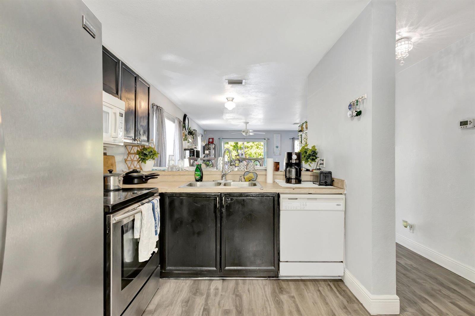 A kitchen features black cabinets, stainless steel appliances, a white dishwasher, and wood-look flooring — 87 Pheasant Run Boulevard, West Palm Beach FL 33415, WEST PALM BEACH, FL