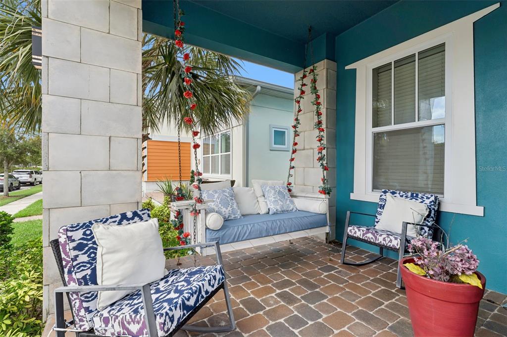 A covered front porch features a hanging daybed, two rocking chairs, and brick flooring — 8033 NEMOURS PARKWAY, ORLANDO, FL