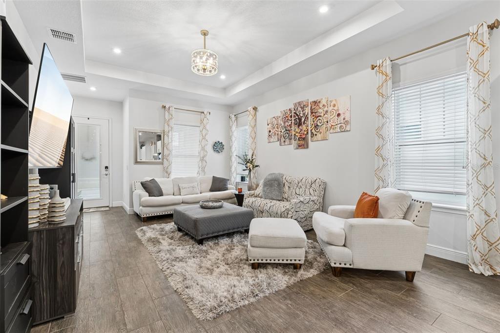 A living room features a tray ceiling, tile flooring, a large area rug, and neutral furniture — 8033 NEMOURS PARKWAY, ORLANDO, FL