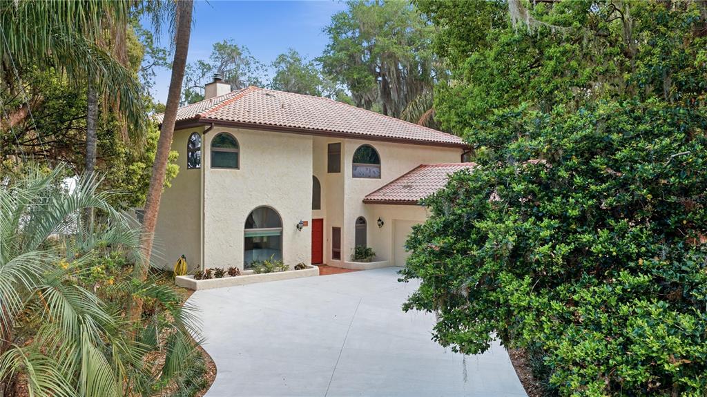 A two-story stucco house with a tile roof and a concrete driveway sits among trees — 12621 SE SUNSET HARBOR ROAD, WEIRSDALE, FL