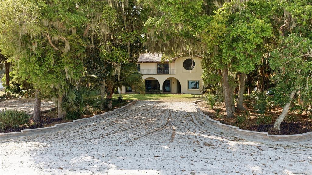 A two-story house with a sand driveway is framed by large, moss-covered oak trees — 12621 SE SUNSET HARBOR ROAD, WEIRSDALE, FL