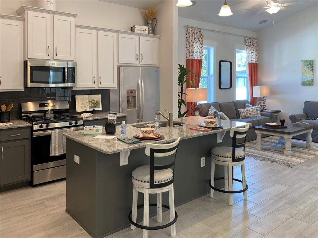 A kitchen with a gray island and white cabinets opens into a living room area — 904 AZALEA WALK CIRCLE, DELAND, FL