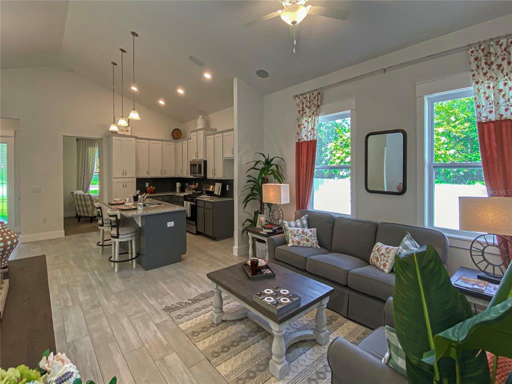 An open-concept living room and kitchen featuring a gray sofa, island, and vaulted ceilings — 904 AZALEA WALK CIRCLE, DELAND, FL