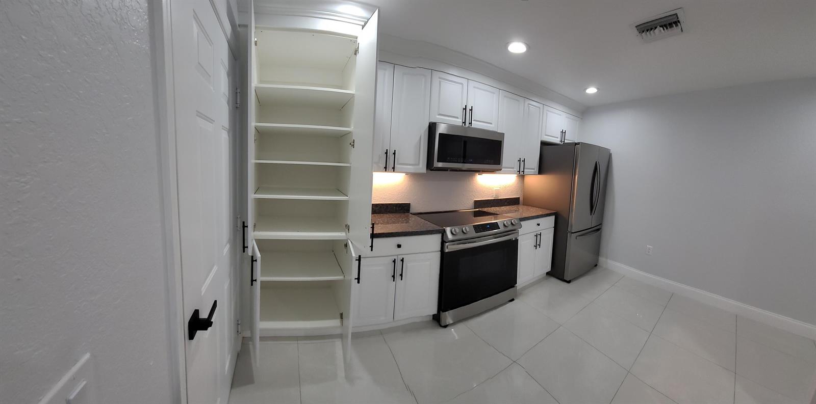A kitchen features white cabinets, stainless steel appliances, dark countertops, and light tile flooring — 1772 N Dovetail Drive # C, Fort Pierce FL 34982, FORT PIERCE, FL