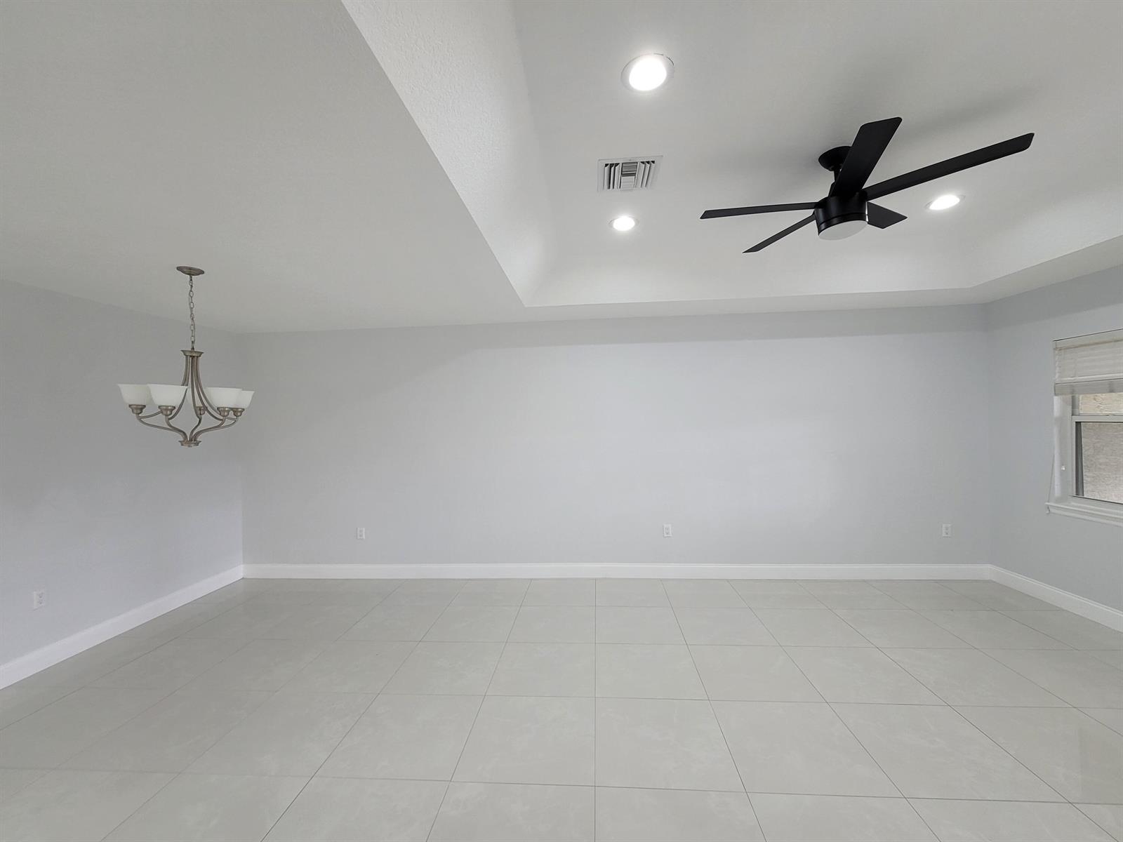 An empty room features light gray walls, large floor tiles, a tray ceiling, and a chandelier — 1772 N Dovetail Drive # C, Fort Pierce FL 34982, FORT PIERCE, FL