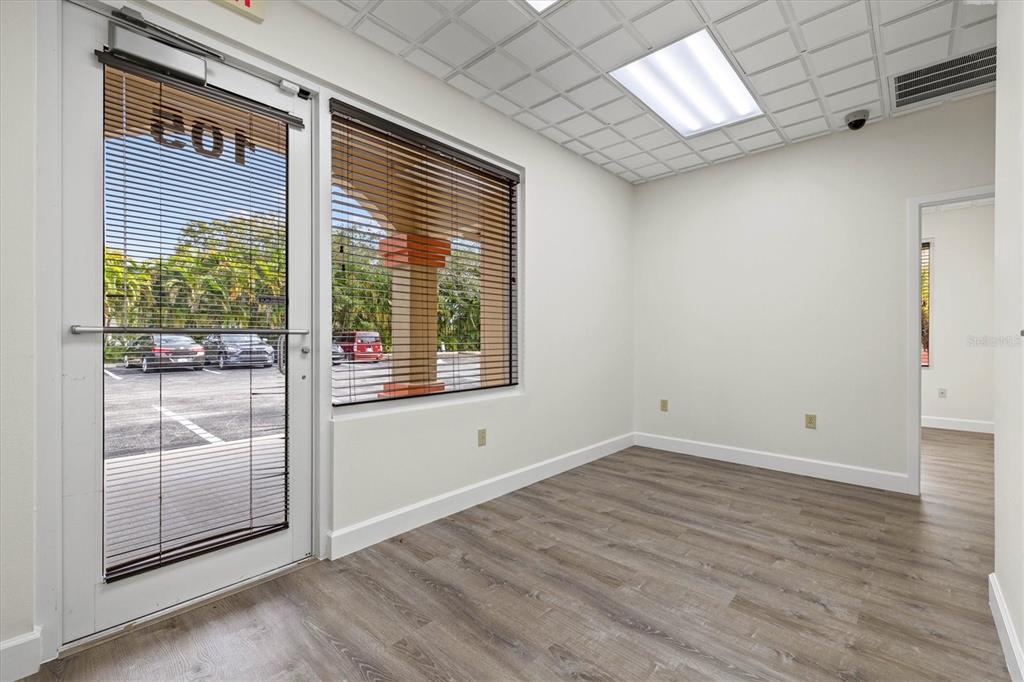 An empty office space features wood-look flooring, white walls, a glass door, and window blinds — 234 N RHODES AVENUE UNIT 105, SARASOTA, FL