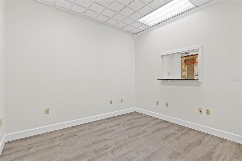 An empty office room features white walls, wood-look flooring, a drop ceiling, and a service window — 234 N RHODES AVENUE UNIT 105, SARASOTA, FL
