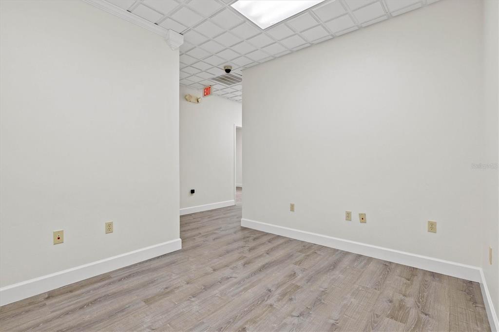 An empty office room features light wood-look flooring, white walls, and a drop ceiling — 234 N RHODES AVENUE UNIT 105, SARASOTA, FL