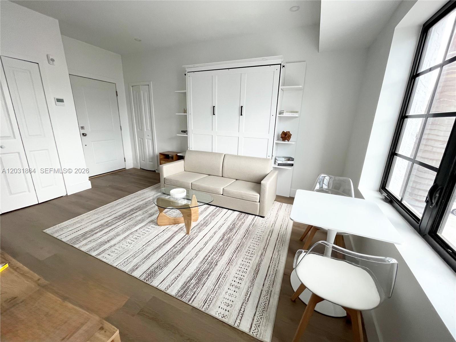 A studio apartment features a white Murphy bed, a beige sofa, and a small dining area — 1619 Jefferson Ave # 107, Miami Beach FL 33139, MIAMI BEACH, FL