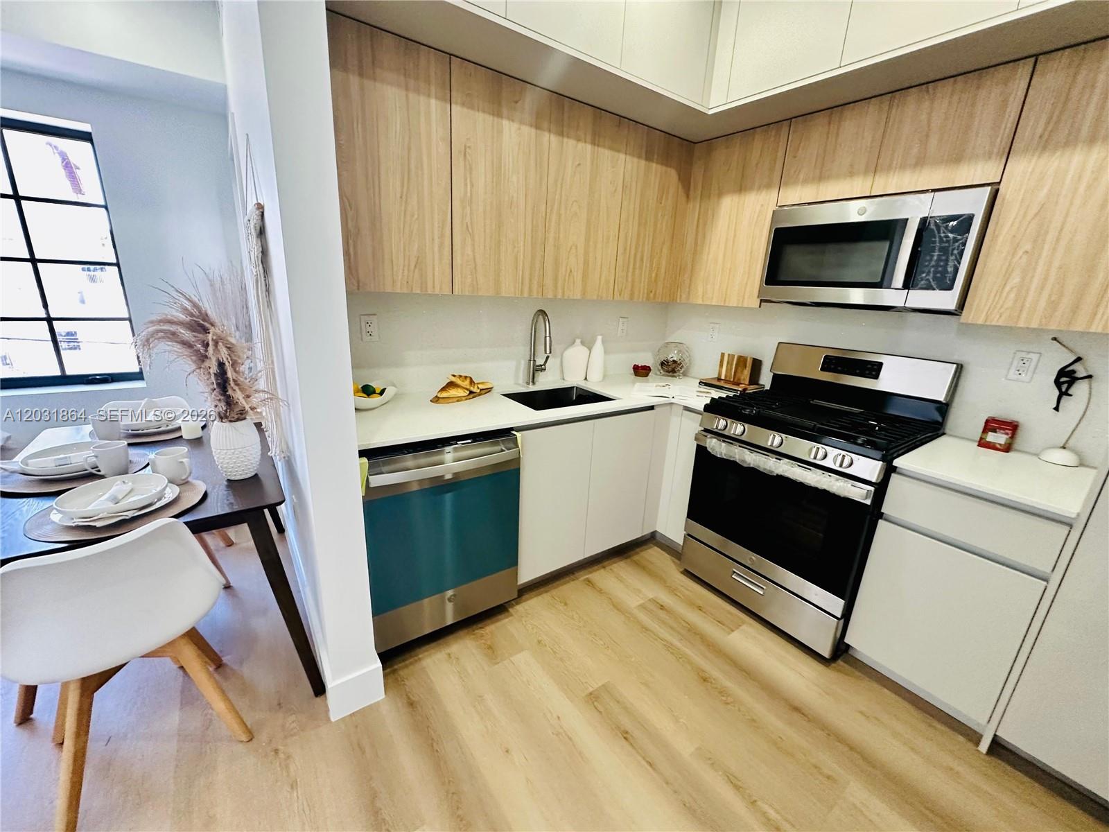A modern kitchen features light wood cabinets, stainless steel appliances, and white countertops — 1619 Jefferson Ave # 107, Miami Beach FL 33139, MIAMI BEACH, FL