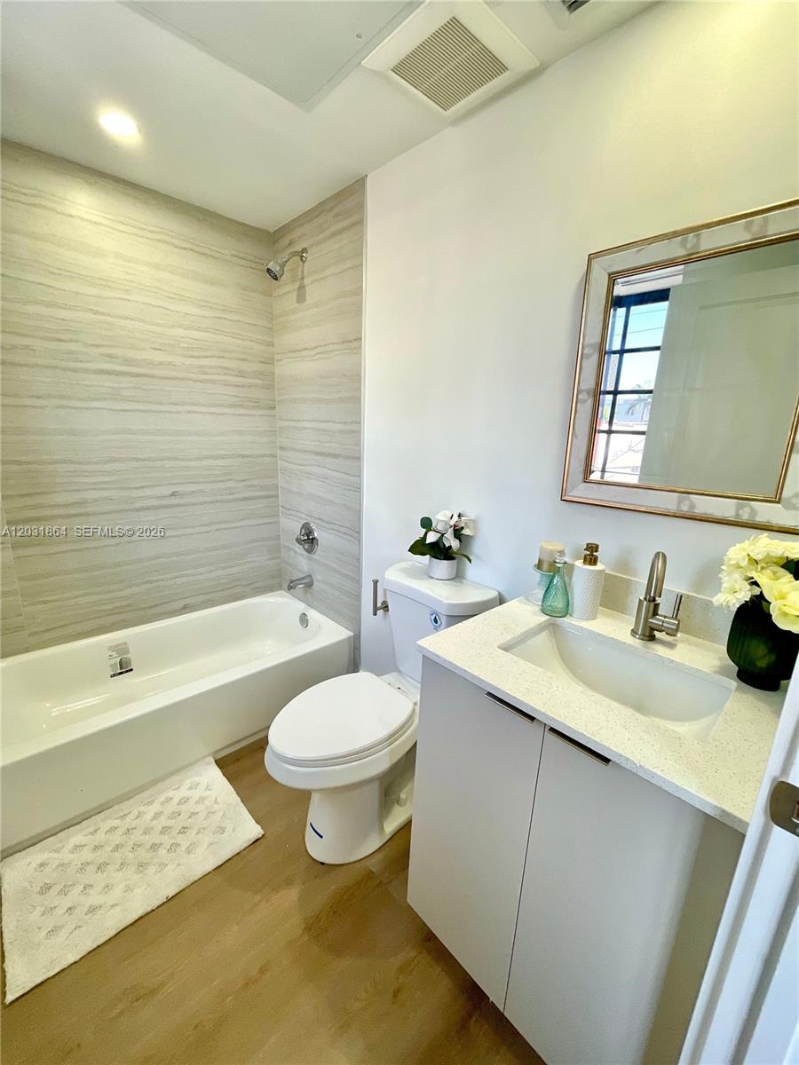 A bathroom features a white vanity, a toilet, and a bathtub with tiled walls — 1619 Jefferson Ave # 107, Miami Beach FL 33139, MIAMI BEACH, FL