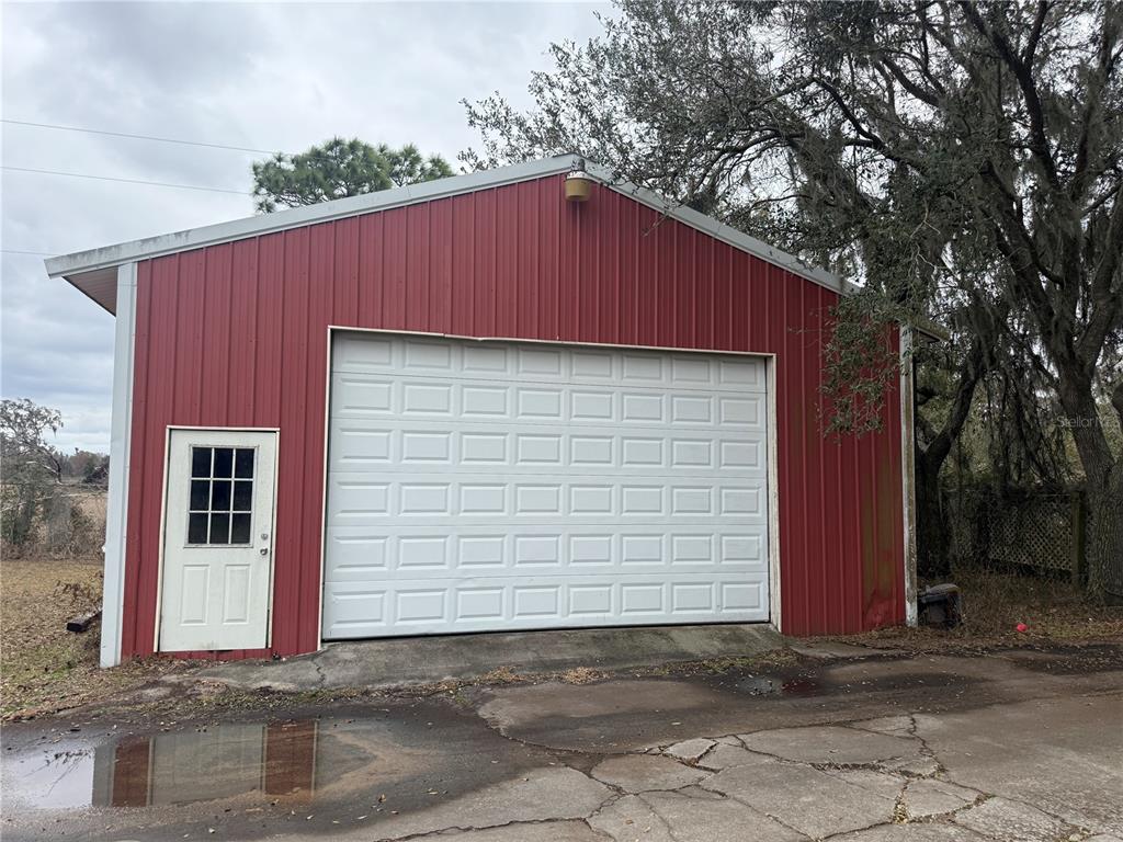 A red metal-sided detached garage with a white roll-up door and a side entry door — 3970 E KNIGHTS GRIFFIN ROAD, PLANT CITY, FL