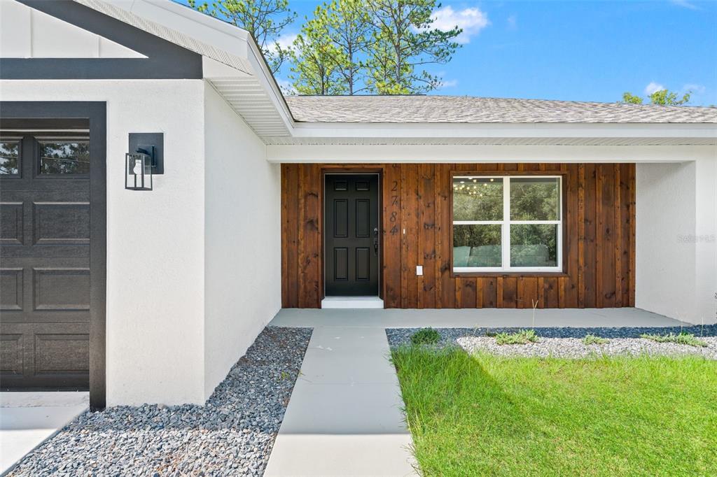 The exterior of a house features a white stucco wall, a dark door, and wood siding — 2784 W PARAGON, CITRUS SPRINGS, FL