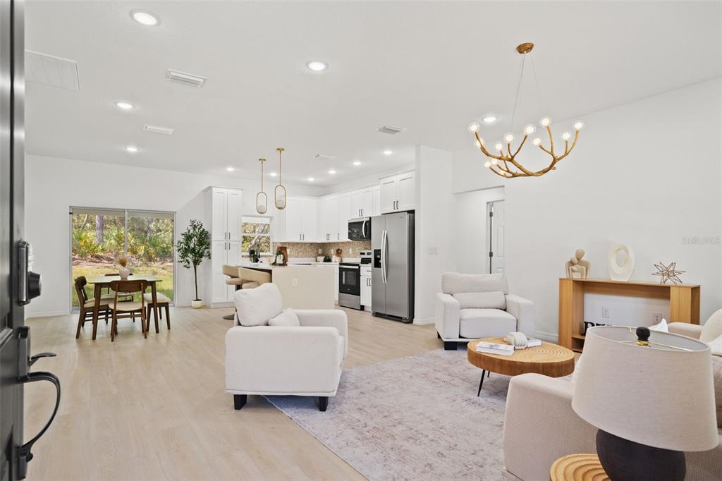 An open-concept living room and kitchen featuring white cabinetry, light wood flooring, and antler lighting — 2784 W PARAGON, CITRUS SPRINGS, FL
