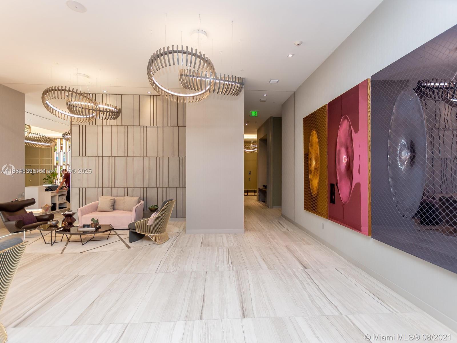 A modern lobby features light wood-look tile flooring, sculptural pendant lighting, and large abstract wall art — 4010 S Ocean Dr # R401, Hollywood FL 33019, HOLLYWOOD, FL