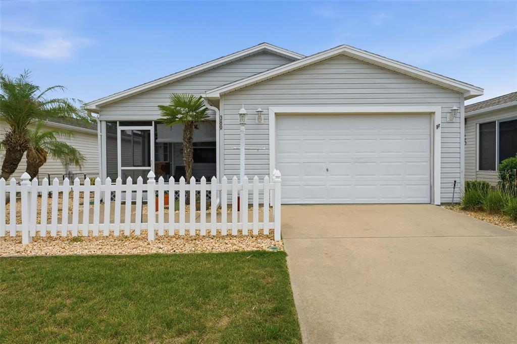 A light gray single-story house features a white garage door and a white picket fence — 389 SEVEN OAKS LANE, THE VILLAGES, FL