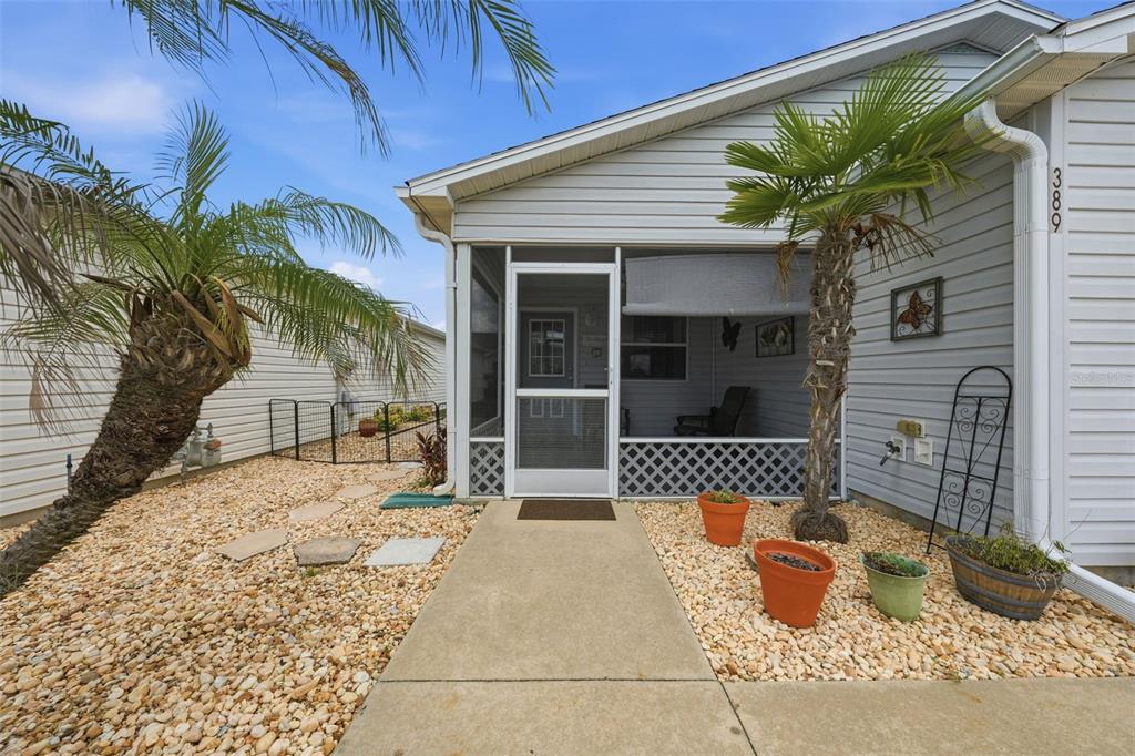 A light-colored house exterior features a screened-in front porch, palm trees, and gravel landscaping — 389 SEVEN OAKS LANE, THE VILLAGES, FL