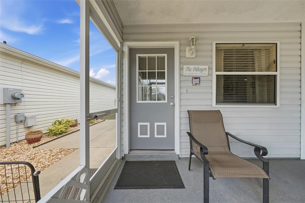 A covered porch features a gray door, a brown chair, and light gray siding — 389 SEVEN OAKS LANE, THE VILLAGES, FL