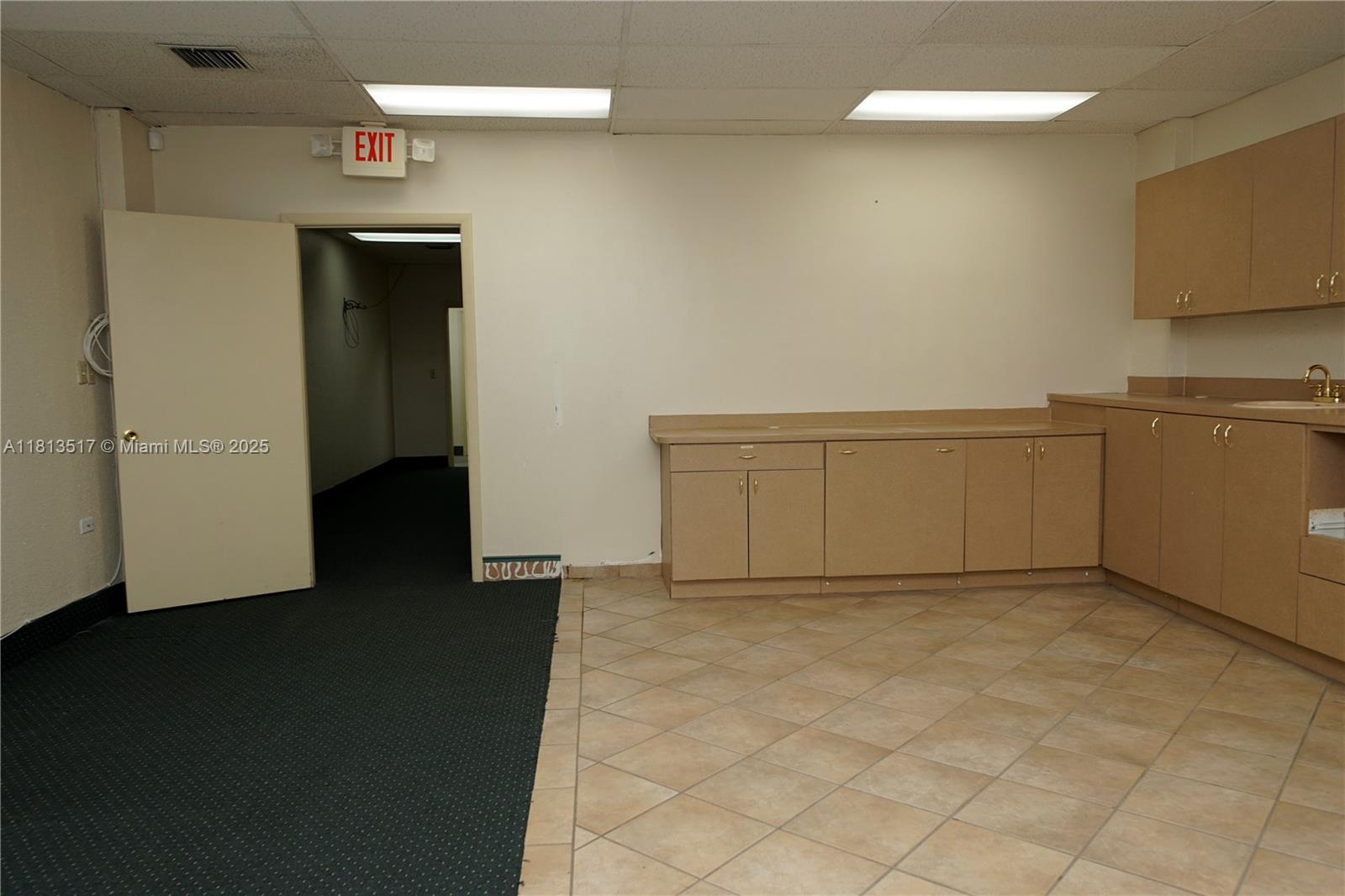 This office space features a kitchenette with tan cabinets, tiled flooring, and an exit door — 8500 SW 40th St, Miami FL 33155, MIAMI, FL
