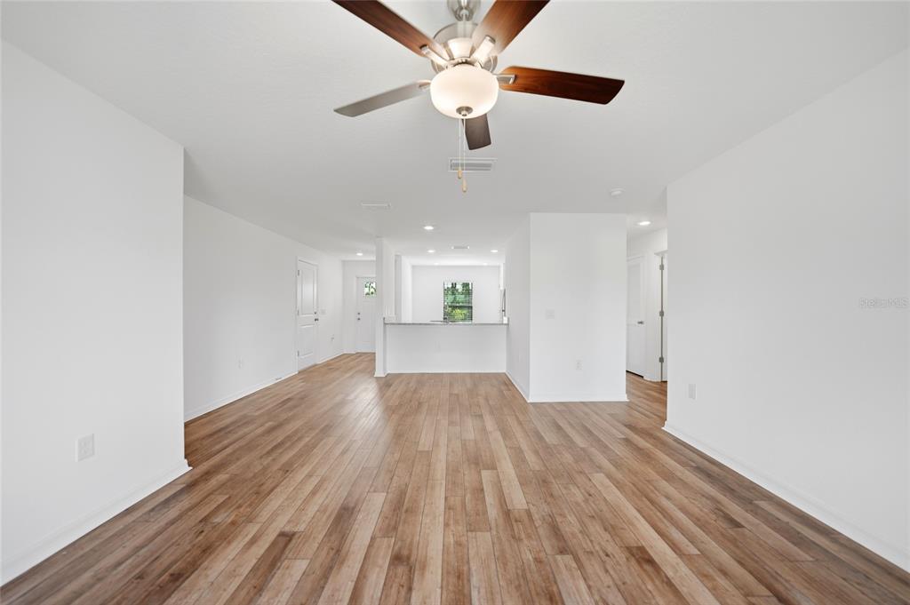 A spacious living room with wood-look flooring, a ceiling fan, and an open kitchen beyond — 5373 ULYSSES STREET, PORT CHARLOTTE, FL