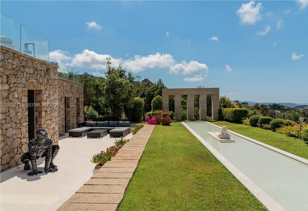 A stone patio with a sculpture overlooks a long reflecting pool and landscaped garden — Sardinia Luxury Estate Porto Cervo Max Mlekus, FL