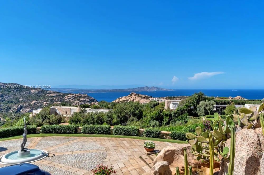 A stone-paved courtyard with a fountain overlooks a coastal landscape with hills and the sea — Sardinia Luxury Estate Porto Cervo Max Mlekus, FL