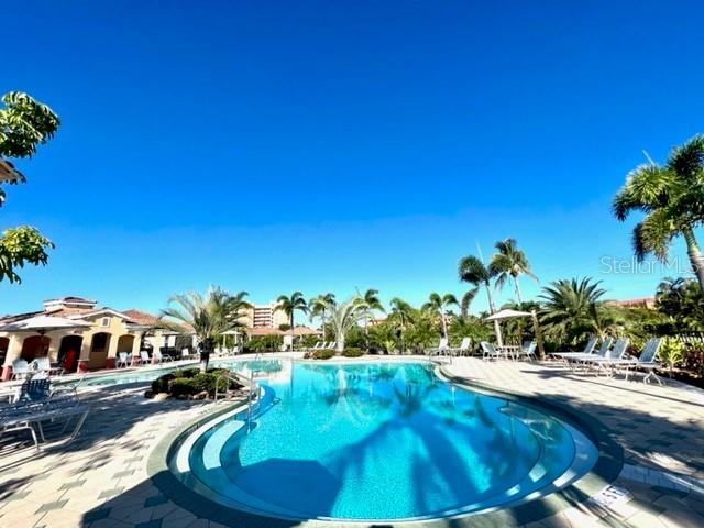 A swimming pool surrounded by a paved deck, palm trees, and residential buildings under a sky — 3181 MATECUMBE KEY ROAD UNIT 10, PUNTA GORDA, FL