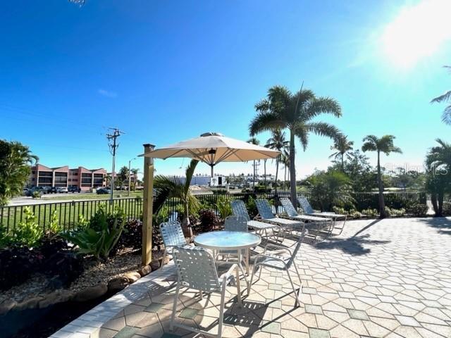 A patio with a table, chairs, and an umbrella overlooks a pool area and palm trees — 3181 MATECUMBE KEY ROAD UNIT 10, PUNTA GORDA, FL