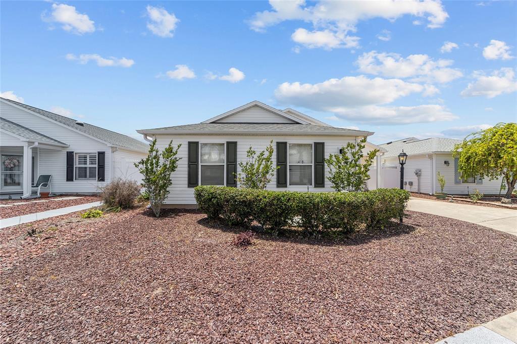 A single-story house with white siding, black shutters, and a gravel front yard — 418 FLOSSMOOR COURT, THE VILLAGES, FL