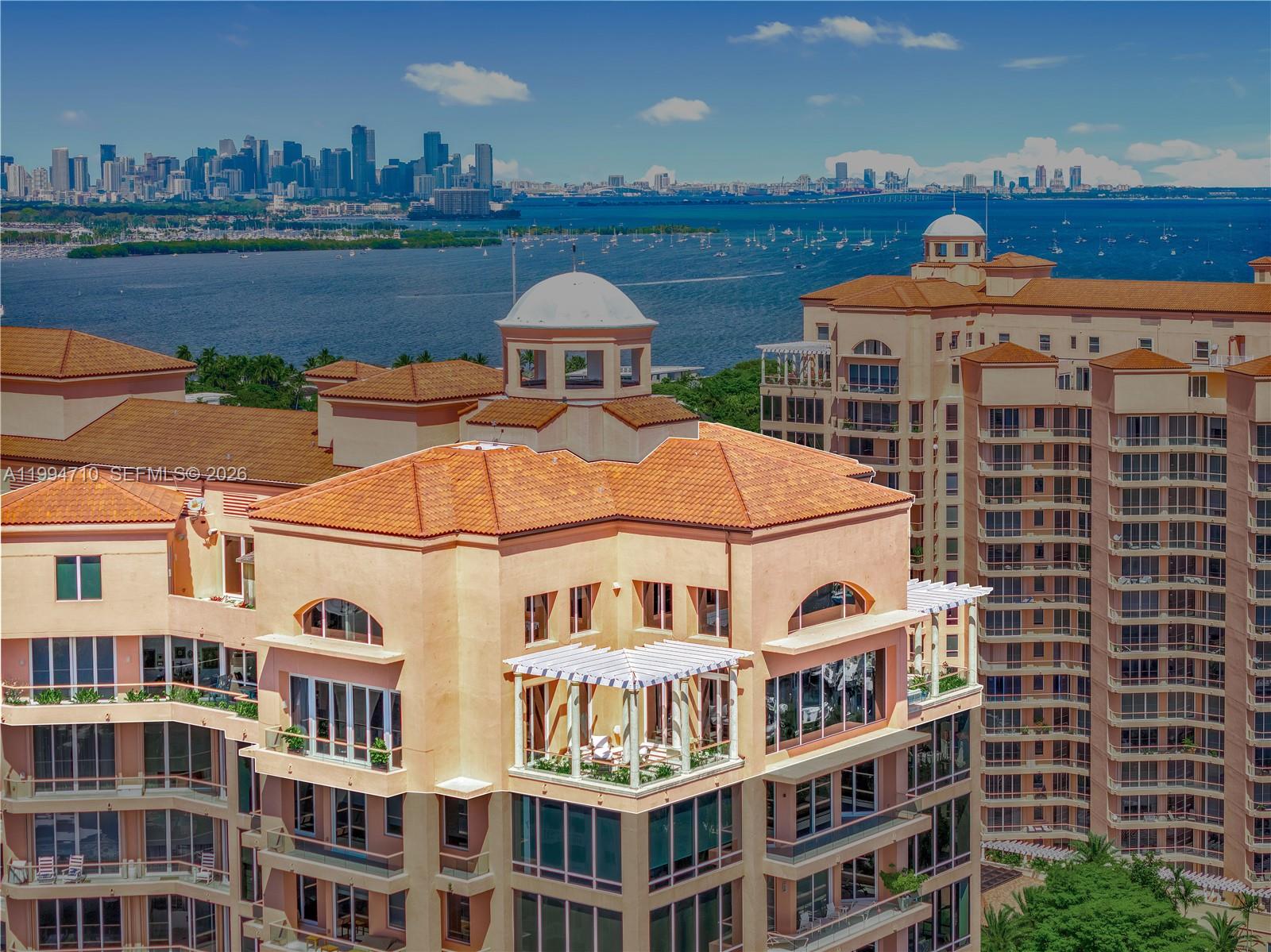 An exterior view of a multi-story building with a rooftop terrace and a city skyline — 60 Edgewater Dr # A, Coral Gables FL 33133, CORAL GABLES, FL