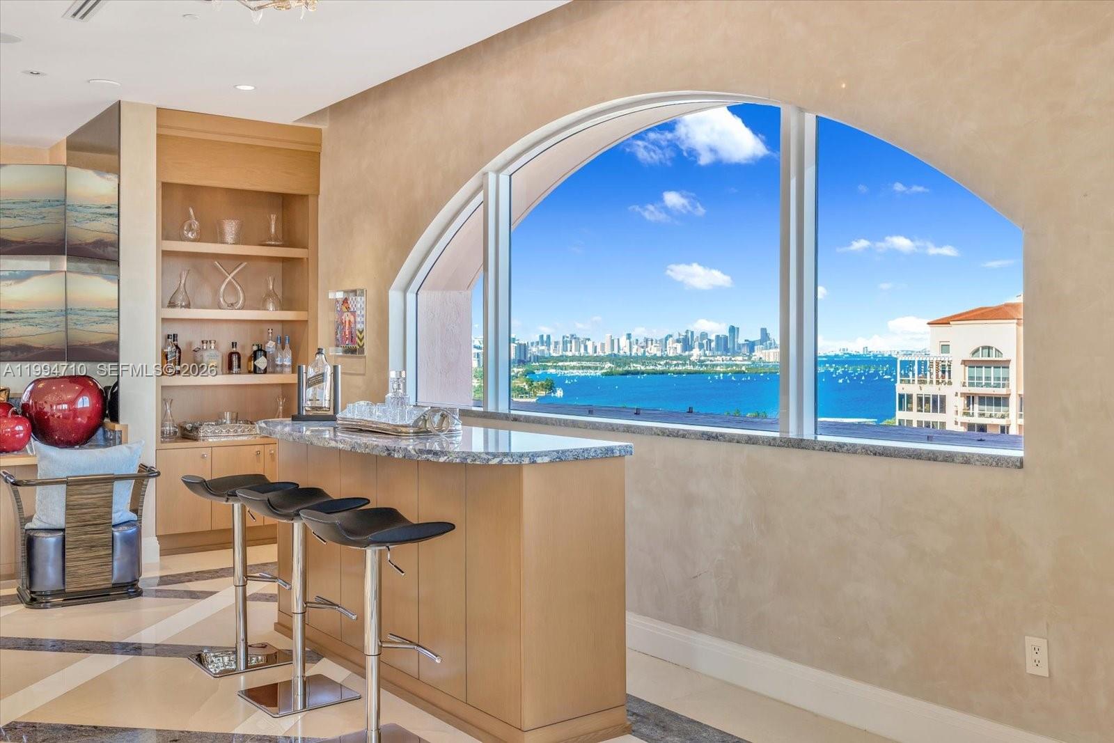 A home bar with stools and built-in shelving overlooks a bay and city skyline — 60 Edgewater Dr # A, Coral Gables FL 33133, CORAL GABLES, FL