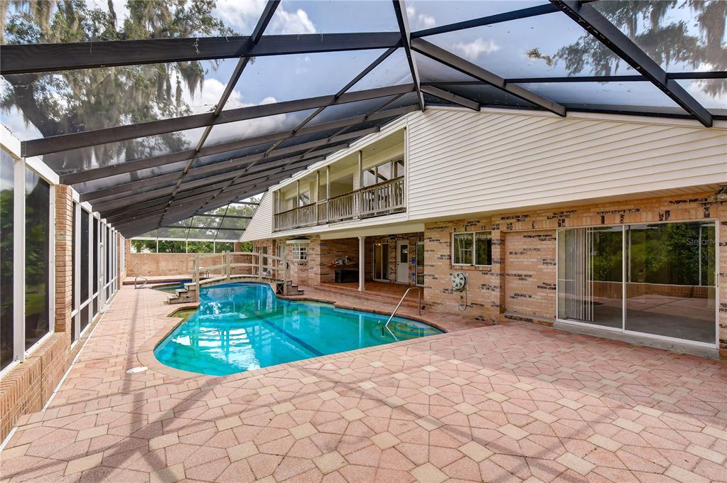 A screened-in pool area with a bridge, brick pavers, and a two-story house exterior — 914 S MILLER ROAD, VALRICO, FL