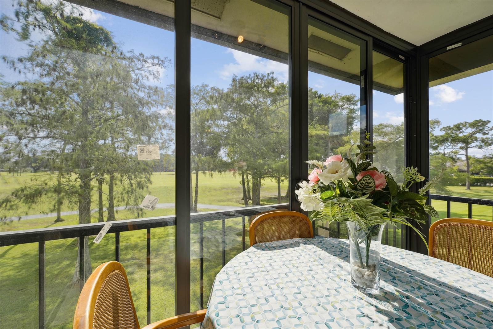 A sunroom with a dining table and chairs overlooks a grassy field with many trees — 21650 Juego Circle # 24b, Boca Raton FL 33433, BOCA RATON, FL