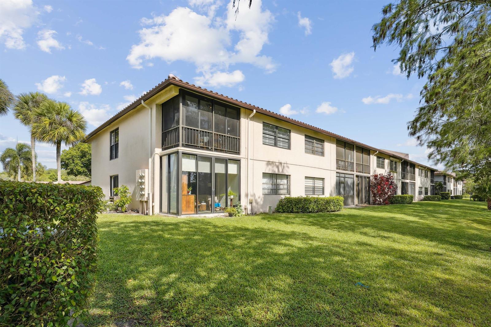 A two-story apartment building with screened balconies and glass sliding doors sits on a lawn — 21650 Juego Circle # 24b, Boca Raton FL 33433, BOCA RATON, FL