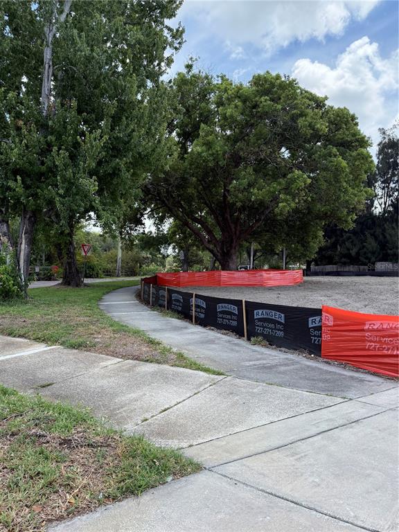 A sidewalk curves past a construction site enclosed by orange and black fencing near trees — 3531 DR MLK JR. DRIVE, ST PETERSBURG, FL