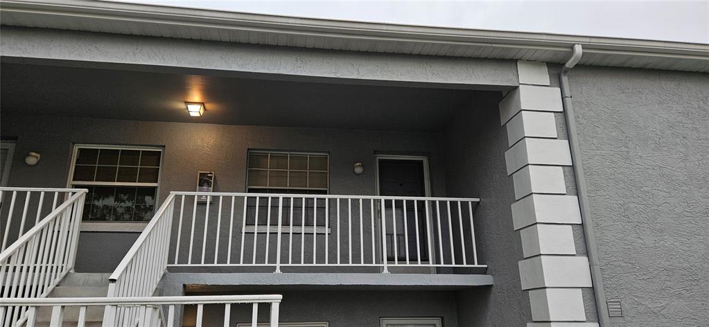 A gray stucco building exterior features a white metal balcony railing and a covered walkway — 12027 HOOSIER COURT UNIT 201, HUDSON, FL