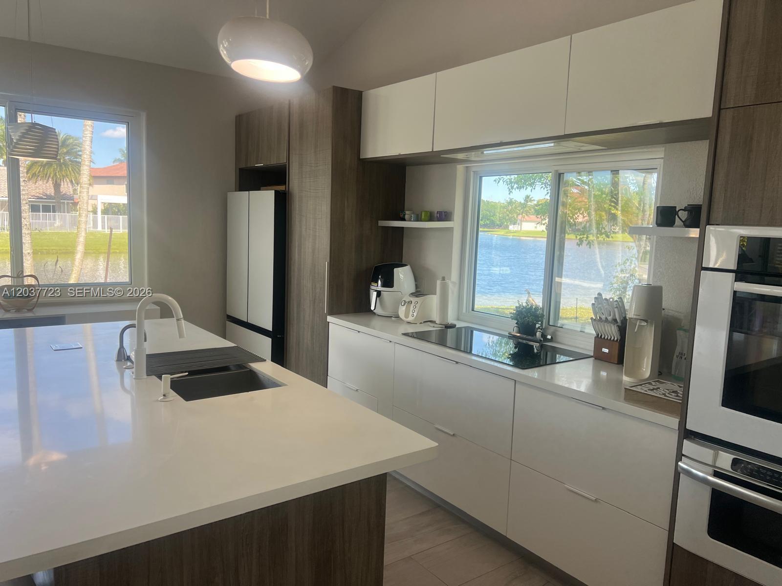 A modern kitchen features white cabinetry, wood-tone accents, a large island, and a lake view — 1130 Spyglass, Weston FL 33326, WESTON, FL