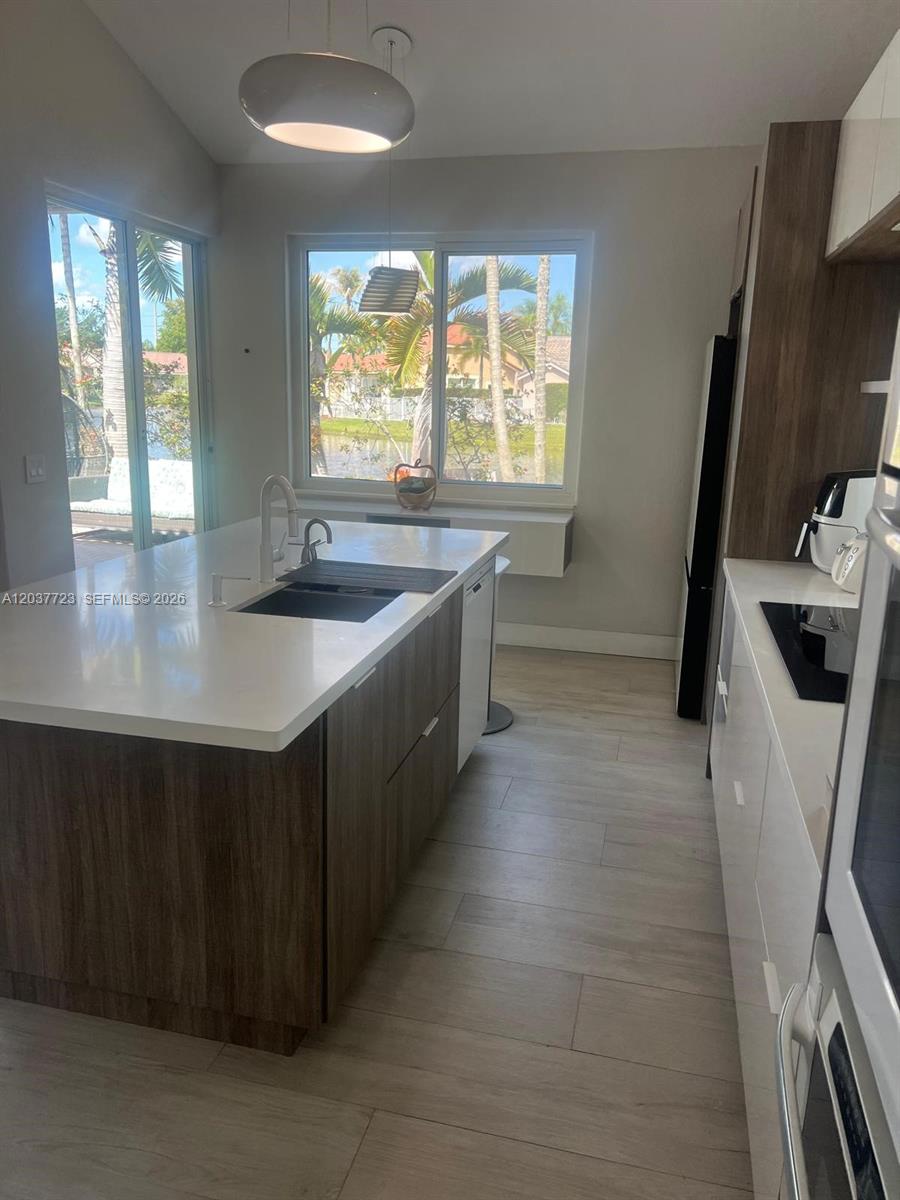 A modern kitchen features a large white island with a sink and wood-toned cabinetry — 1130 Spyglass, Weston FL 33326, WESTON, FL