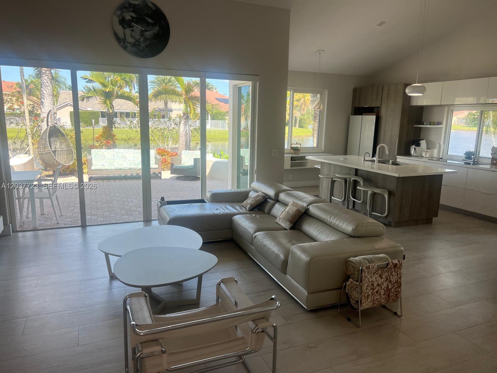 An open-concept living room and kitchen feature a leather sectional, white tables, and sliding doors — 1130 Spyglass, Weston FL 33326, WESTON, FL