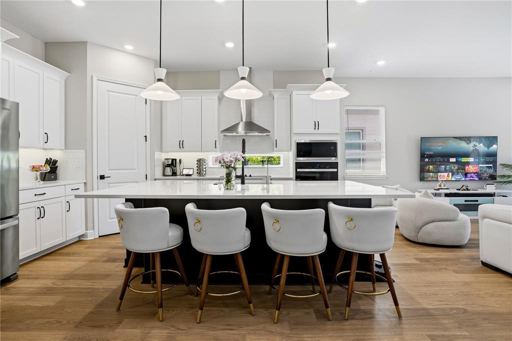 A modern kitchen features a large black island with four white bar stools and white cabinetry — 10156 BALLAST DRIVE, ORLANDO, FL