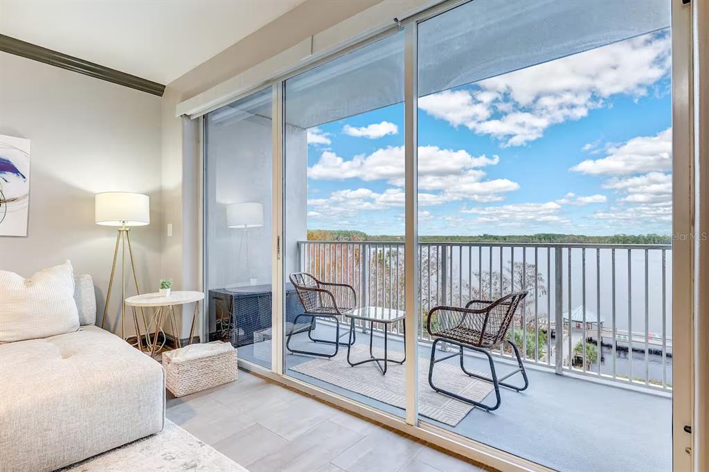 A living room with a sofa and floor lamp opens to a balcony overlooking a lake — 13415 BLUE HERON BEACH DRIVE UNIT 410, ORLANDO, FL