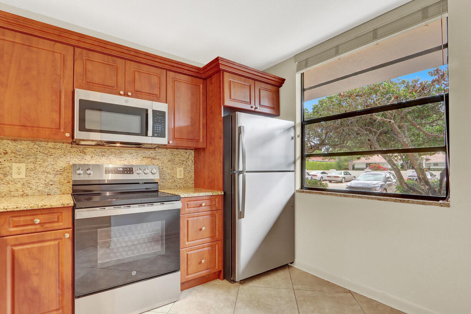 A kitchen features cherry wood cabinets, granite countertops, stainless steel appliances, and a large window — 3636 WHITEHALL Drive # 105, West Palm Beach FL 33401, WEST PALM BEACH, FL
